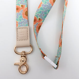 Floral patterned lanyard with a beige strap and gold clasp on a light gray background