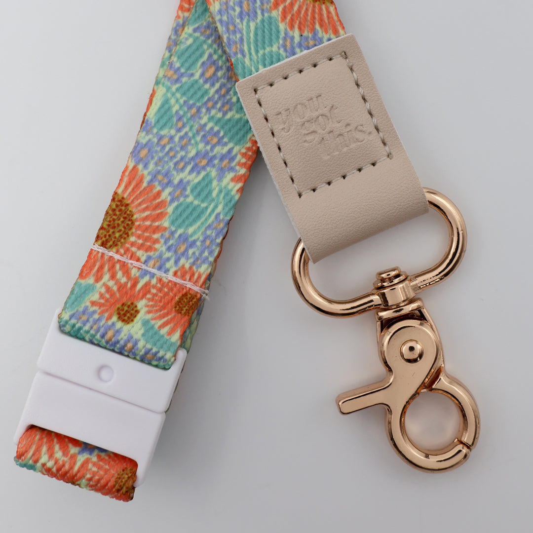 Floral patterned lanyard with beige leather strap and rose gold clasp on a light gray background