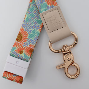 Floral patterned lanyard with beige leather strap and rose gold clasp on a light gray background