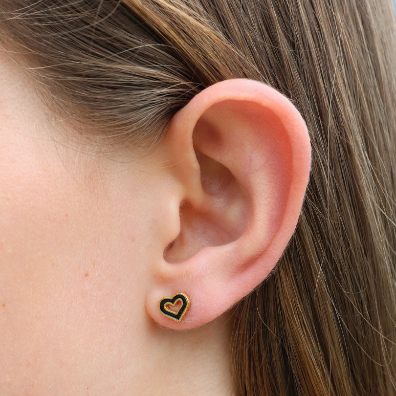 Close-up of an ear wearing a heart-shaped earring with a black border.