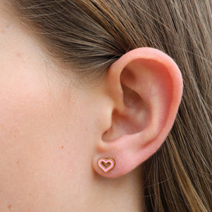 Heart-shaped earring worn on a person's ear with a neutral background