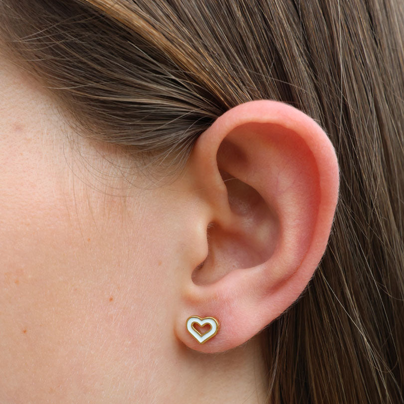 Close-up of an ear wearing a heart-shaped earring with gold border and white center.