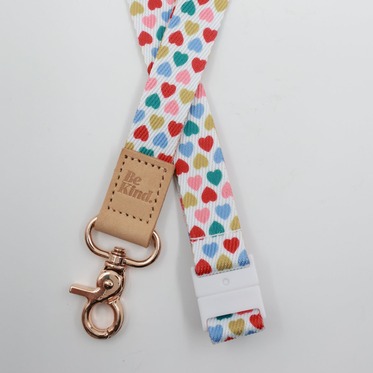Be Kind embossed on a white lanyard with multicoloured hearts and tan trim and a lobster clasp.