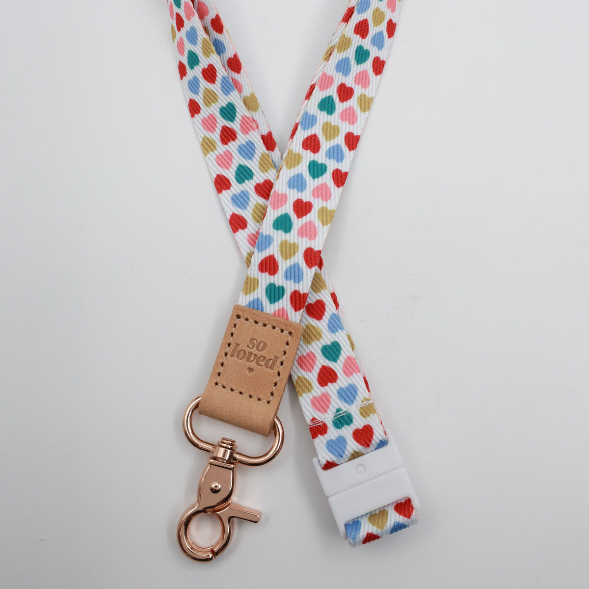 So Loved embossed on a white lanyard with multicoloured hearts and tan trim and a lobster clasp.
