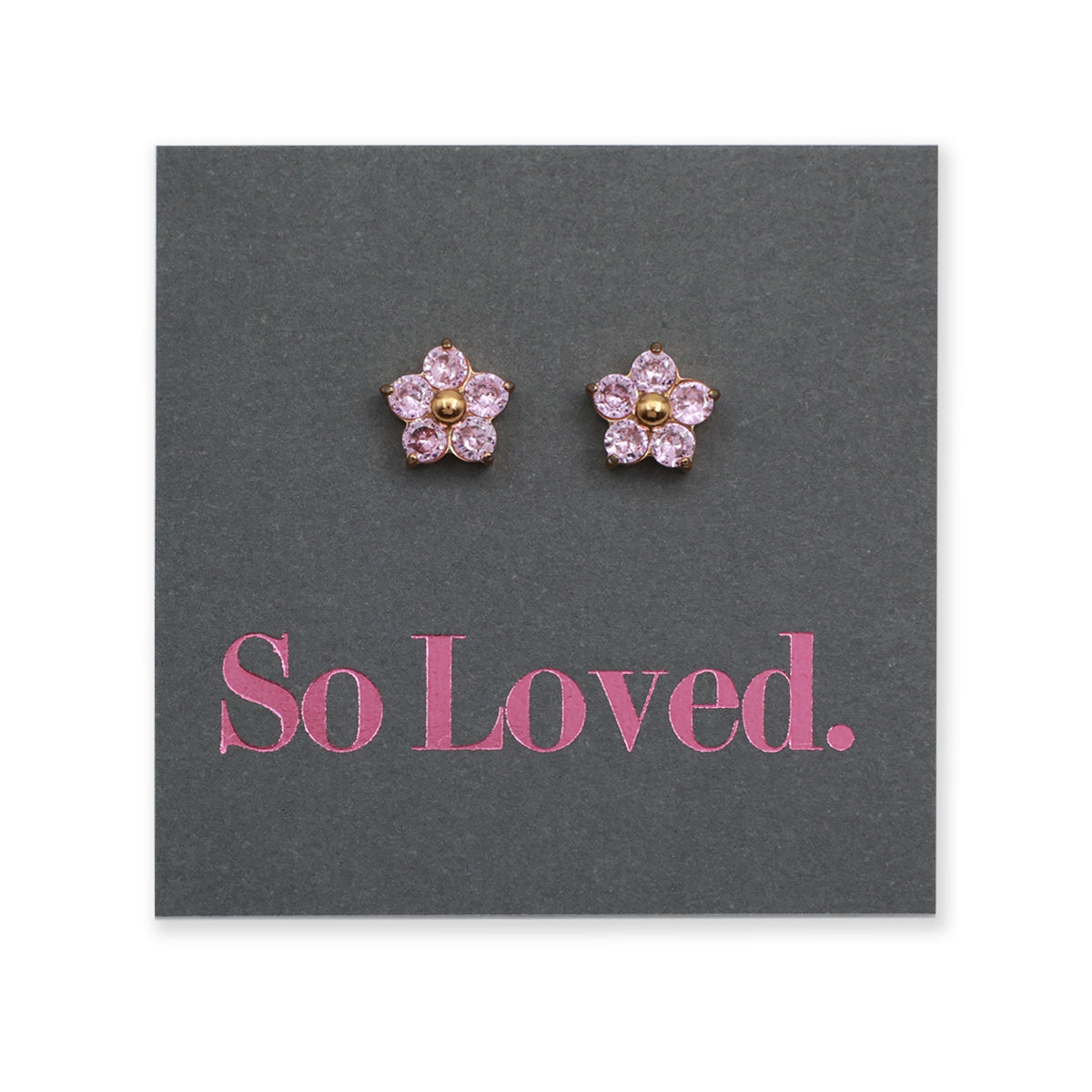 A pair of flower-shaped stud earrings with pink faceted stones and gold centers, displayed on a dark gray card printed with the pink text 'So Loved.'.
