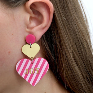 Heart-shaped earrings with pink and gold design worn by a person