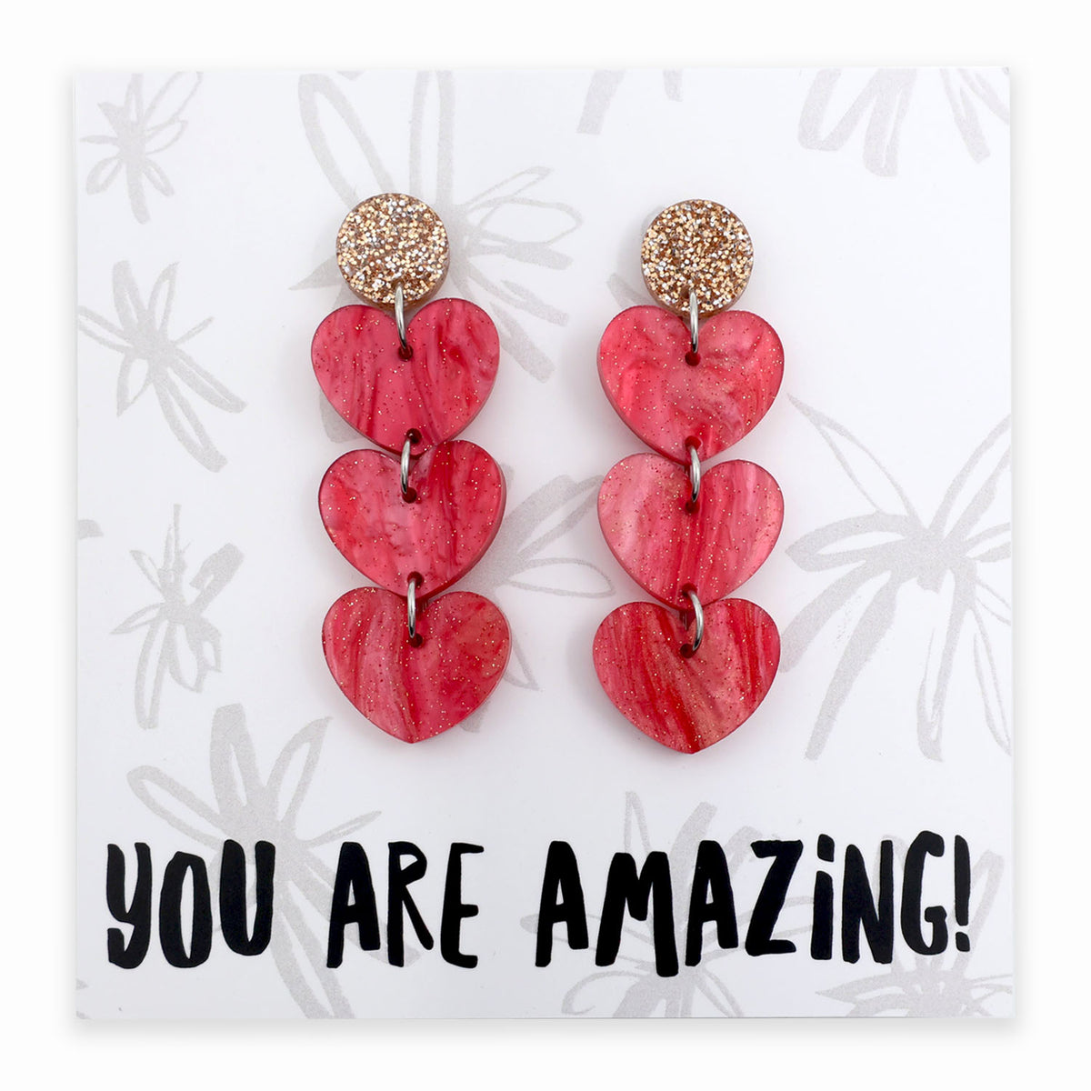 Red heart-shaped earrings on a card with 'YOU ARE AMAZING!' text