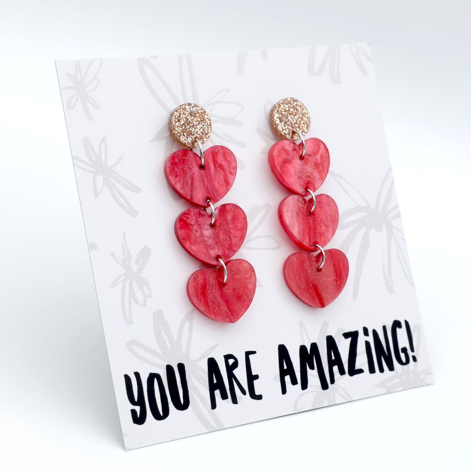 Red heart-shaped earrings on a card with 'YOU ARE AMAZING!' text