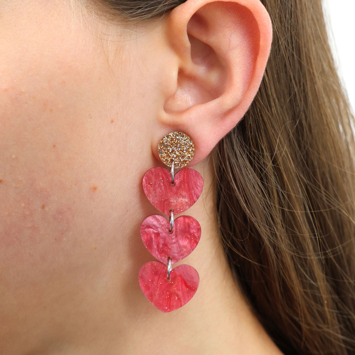 Close-up of an ear wearing a pink heart-shaped earring with a gold accent.