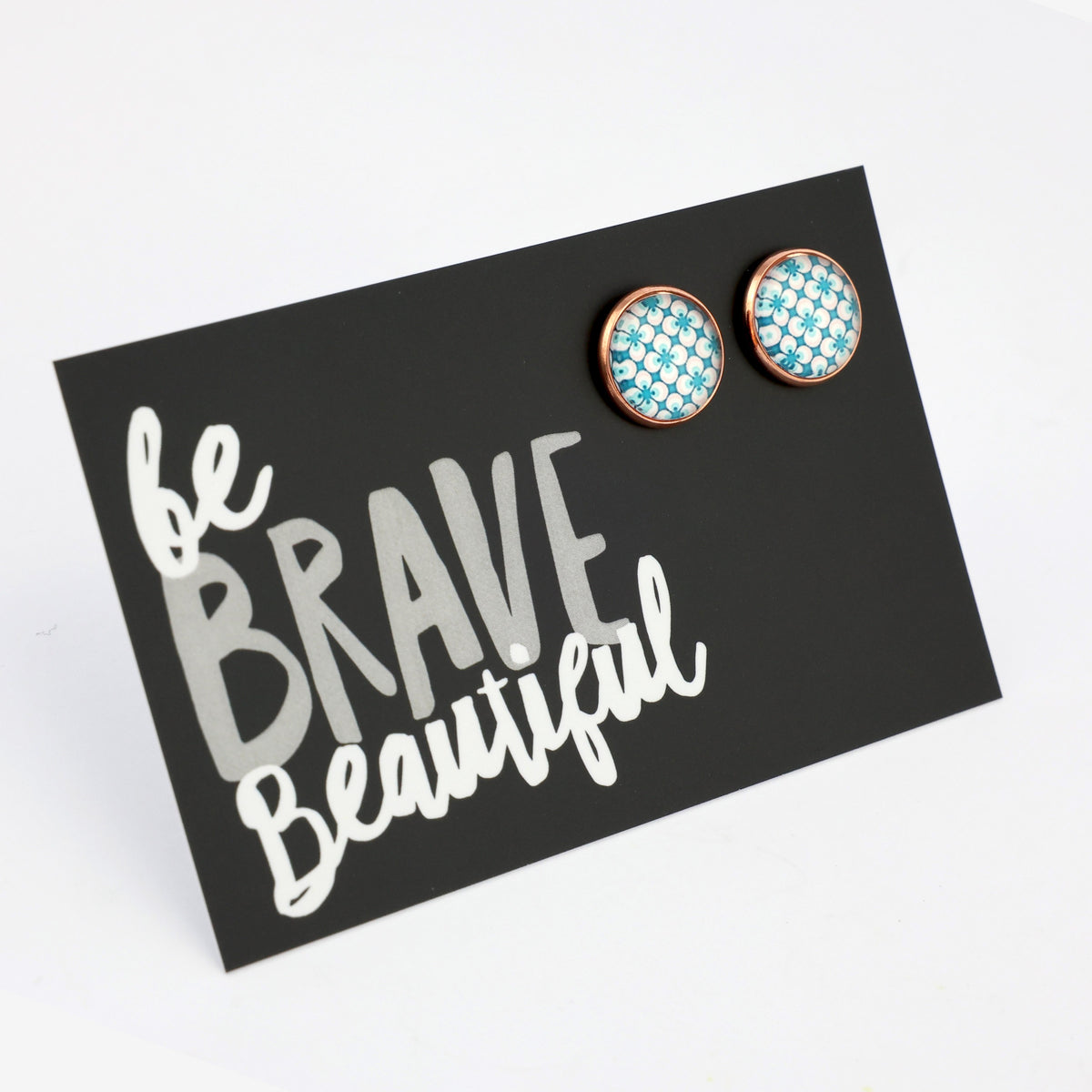 Teal print rose gold stud earrings on brave inspiring word card on white background.