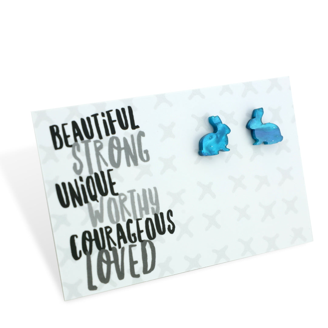 A pair of teal blue acrylic bunny stud earrings on a white display card with the words 'BEAUTIFUL STRONG UNIQUE WORTHY COURAGEOUS LOVED' written at the top.