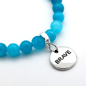 Blue beaded bracelet with a silver 'BRAVE' charm on a white background