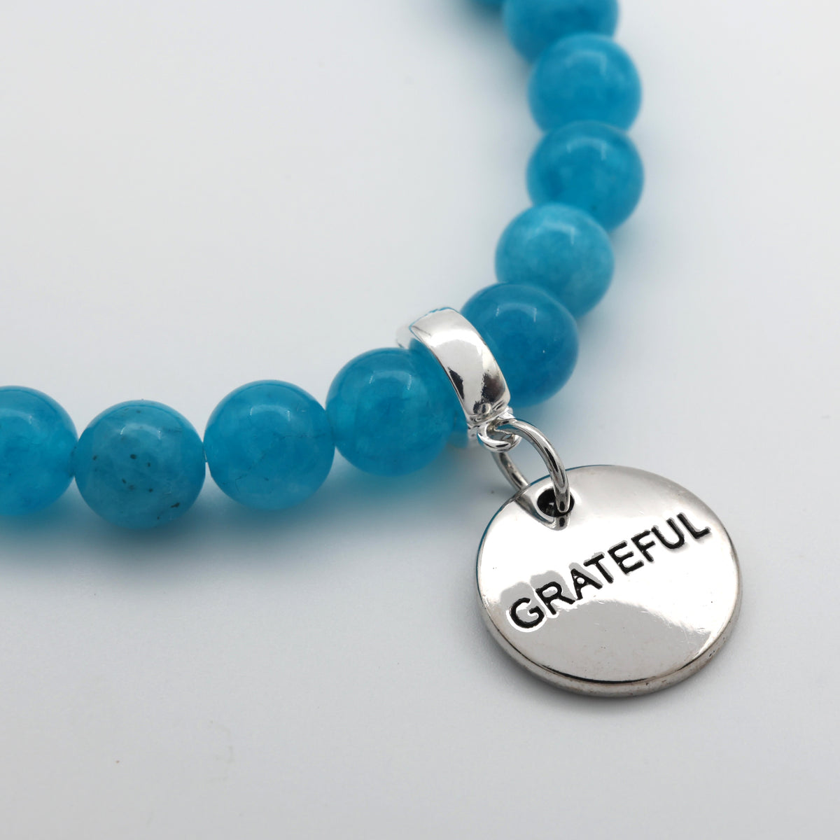 Blue beaded bracelet with a silver 'GRATEFUL' charm on a light gray background