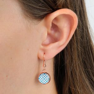 Close-up of an ear wearing a blue patterned earring with a white background
