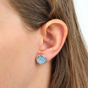 Close-up of an ear wearing a blue patterned stud earring with a blurred background