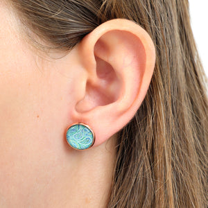Close-up of an ear wearing a round turquoise earring with a paisley design.