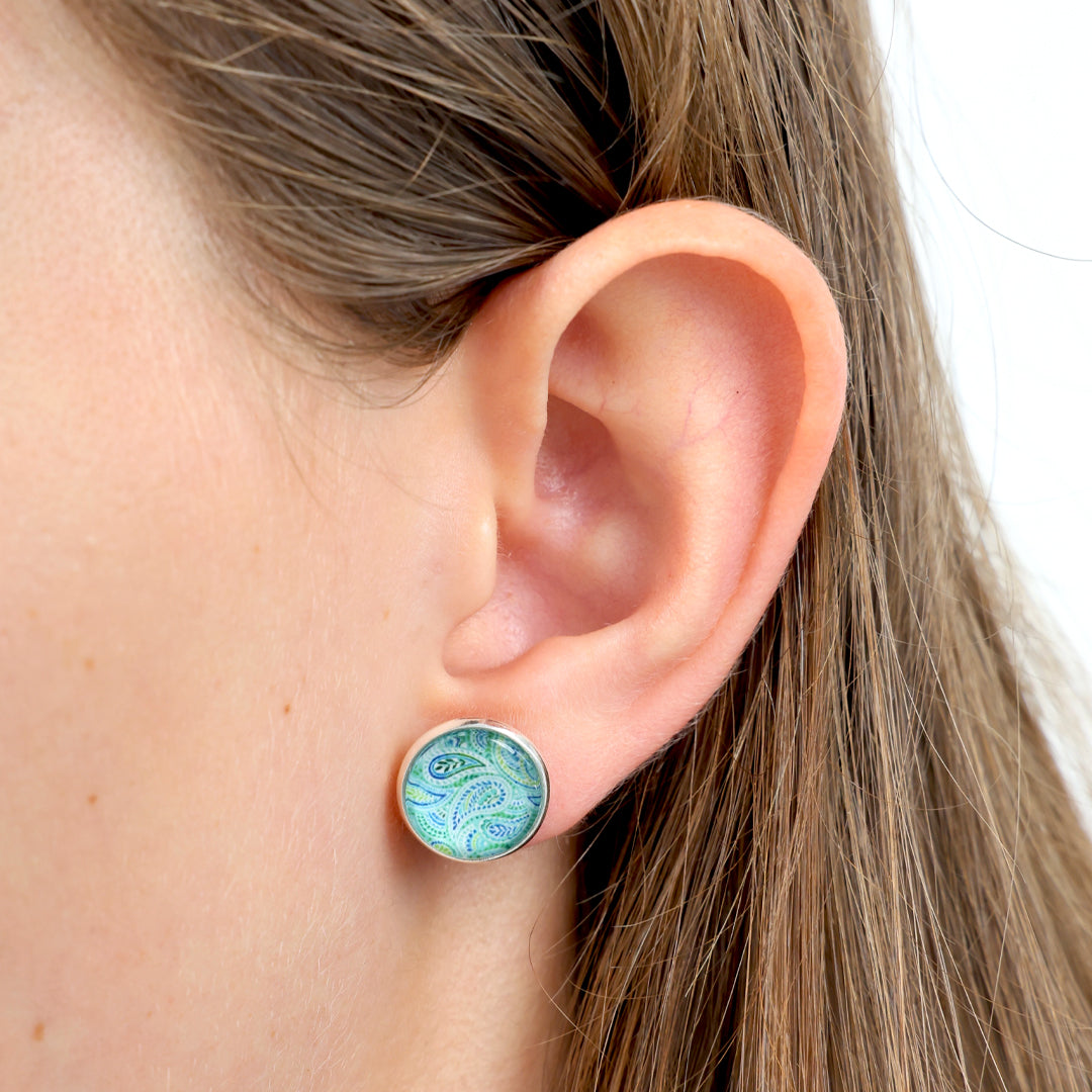 Close-up of an ear wearing a round earring with a paisley design.