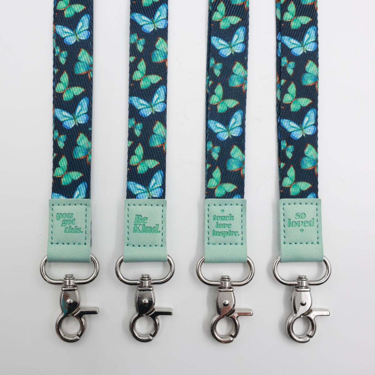 Teal Butterflies lanyards showing Be Kind, Teach Love Inspire, You Got This and So Loved embossed trims and lobster clasps.