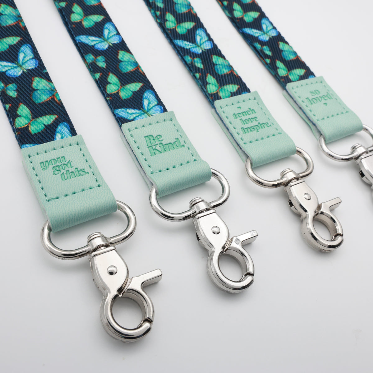 Teal Butterflies lanyards showing Be Kind, Teach Love Inspire, You Got This and So Loved embossed trims and lobster clasps.
