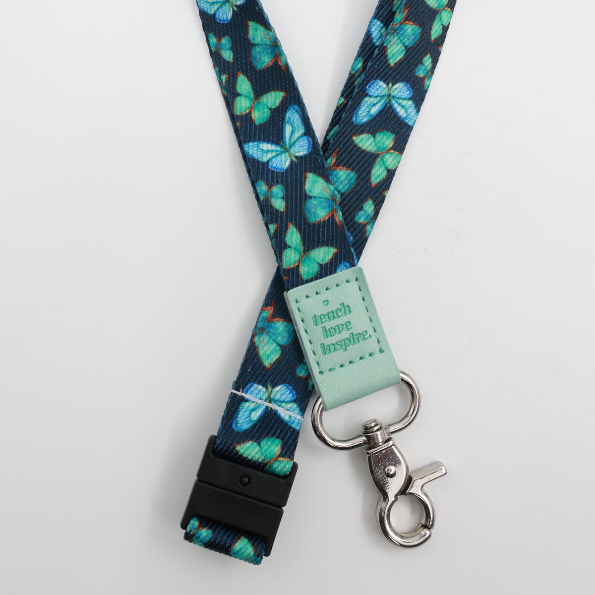 Teach Love Inspire embossed on a navy lanyard with teal butterflies and mint trim and a lobster clasp.
