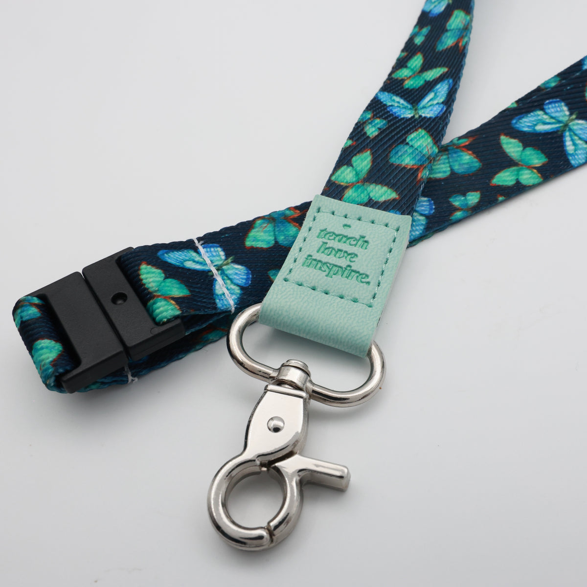 Teach Love Inspire embossed on a navy lanyard with teal butterflies and mint trim and a lobster clasp.