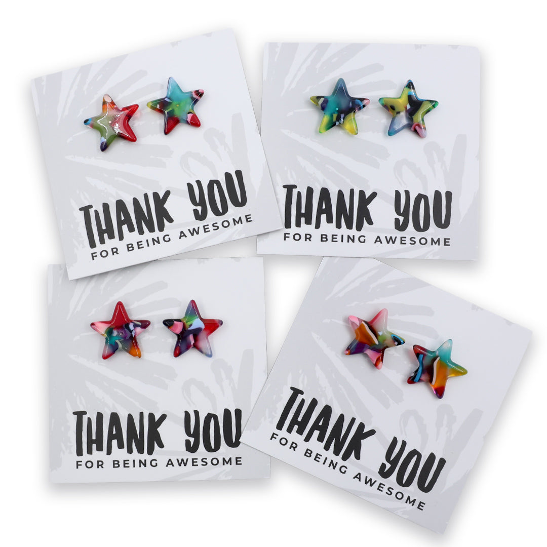 Four star-shaped stud earrings displayed on white backing cards that read 'THANK YOU FOR BEING AWESOME.' The earrings have a multicolor tie-dye pattern with shades of blue, green, pink, orange, and purple.