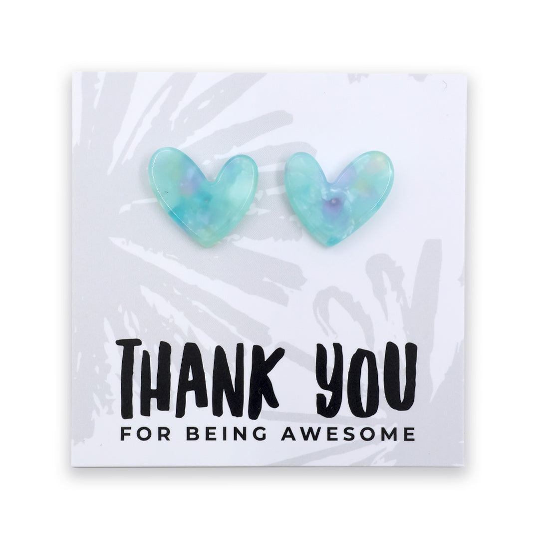 A pair of heart-shaped stud earrings in a translucent light blue and mint green resin with subtle purple swirls, displayed on a white card that reads 'THANK YOU FOR BEING AWESOME'.