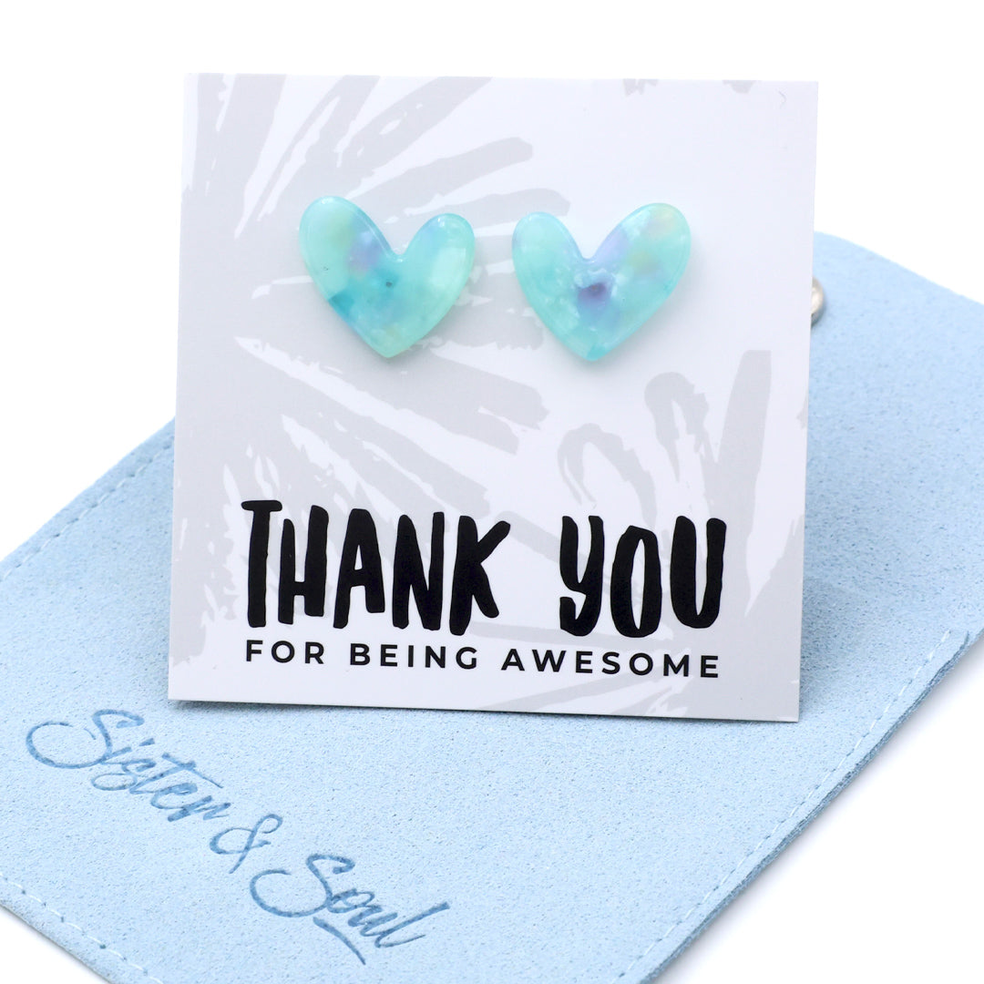 Heart-shaped light blue and green iridescent stud earrings displayed on a white card that reads 'THANK YOU FOR BEING AWESOME,' resting on a light blue fabric pouch with 'Soul & Soul' written in blue script.
