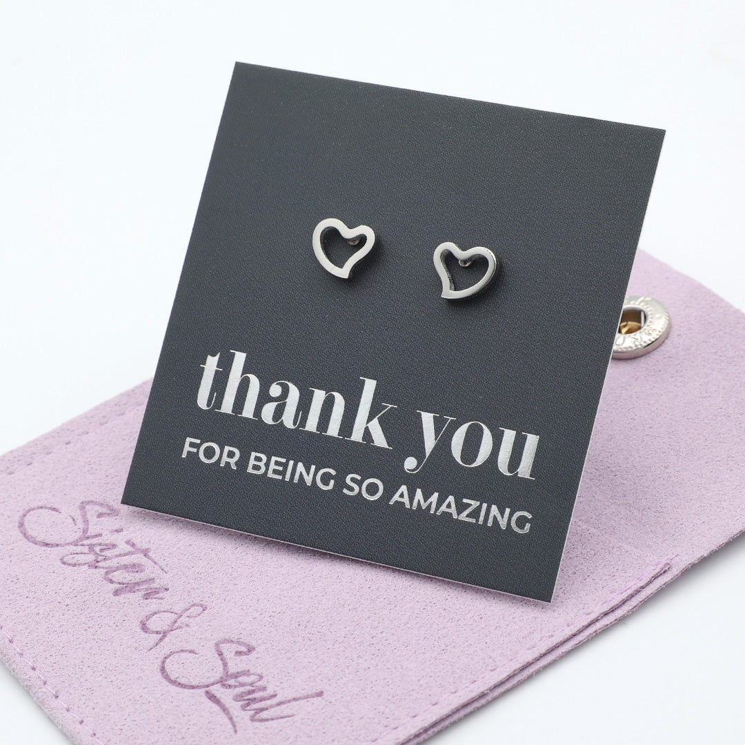 Heart-shaped earrings on a 'thank you' card with a pink pouch underneath