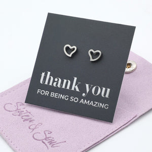 Heart-shaped earrings on a 'thank you' card with a pink pouch underneath