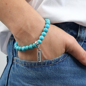 Turquoise beaded bracelet with a silver 'INSPIRE' tag on a wrist, worn with blue jeans.