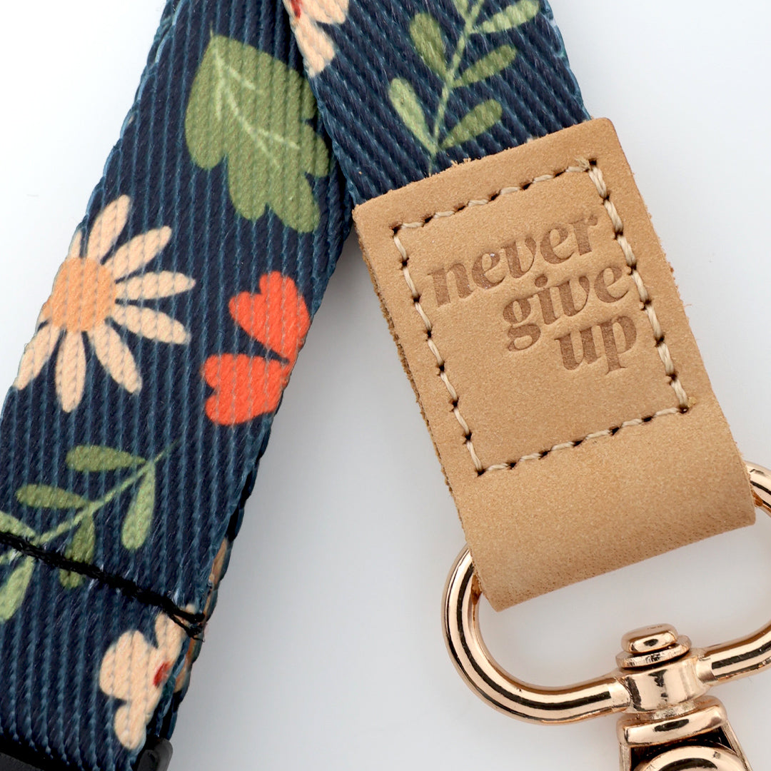 Floral-patterned strap with 'never give up' tag and gold keychain on white background