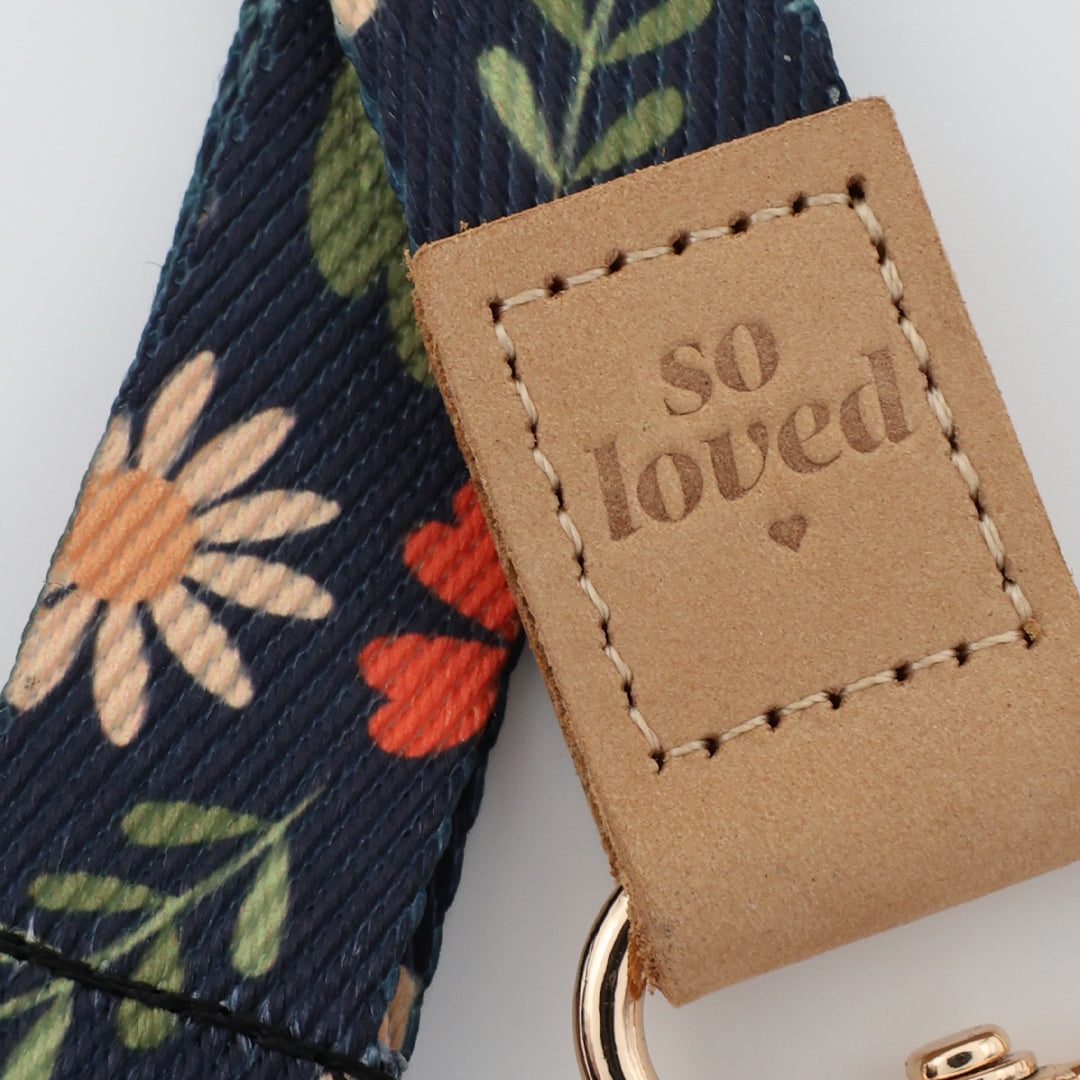 Floral-patterned strap with a 'so loved' tag on a light gray background