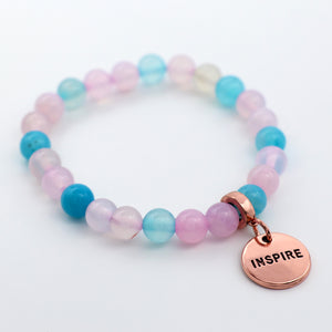 Multicolored beaded bracelet with a 'INSPIRE' charm on a white background