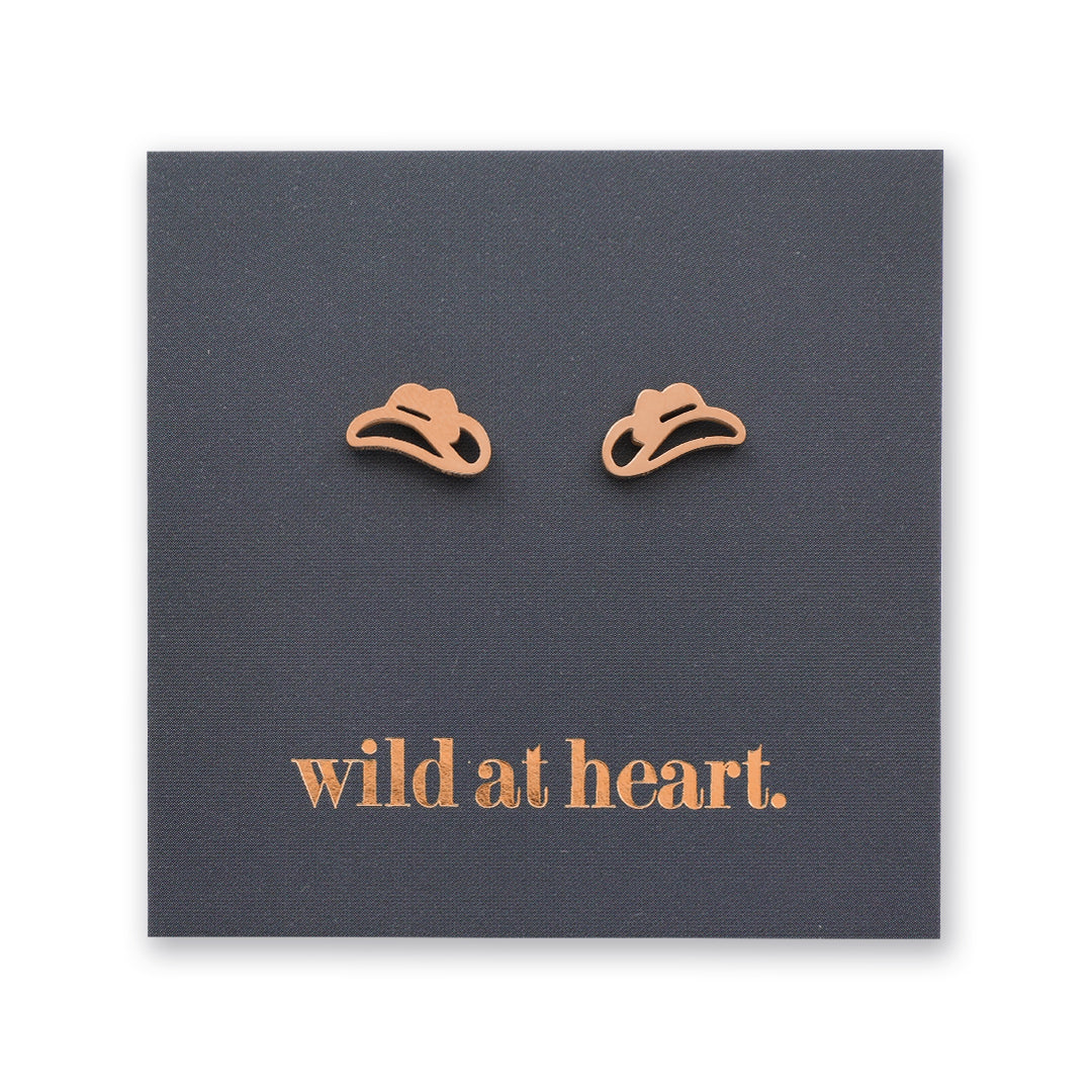 Rose gold cowgirl hat earrings on a black card with 'wild at heart.' text