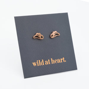 Rose gold cowgirl hat earrings on a black card with 'wild at heart.' text.