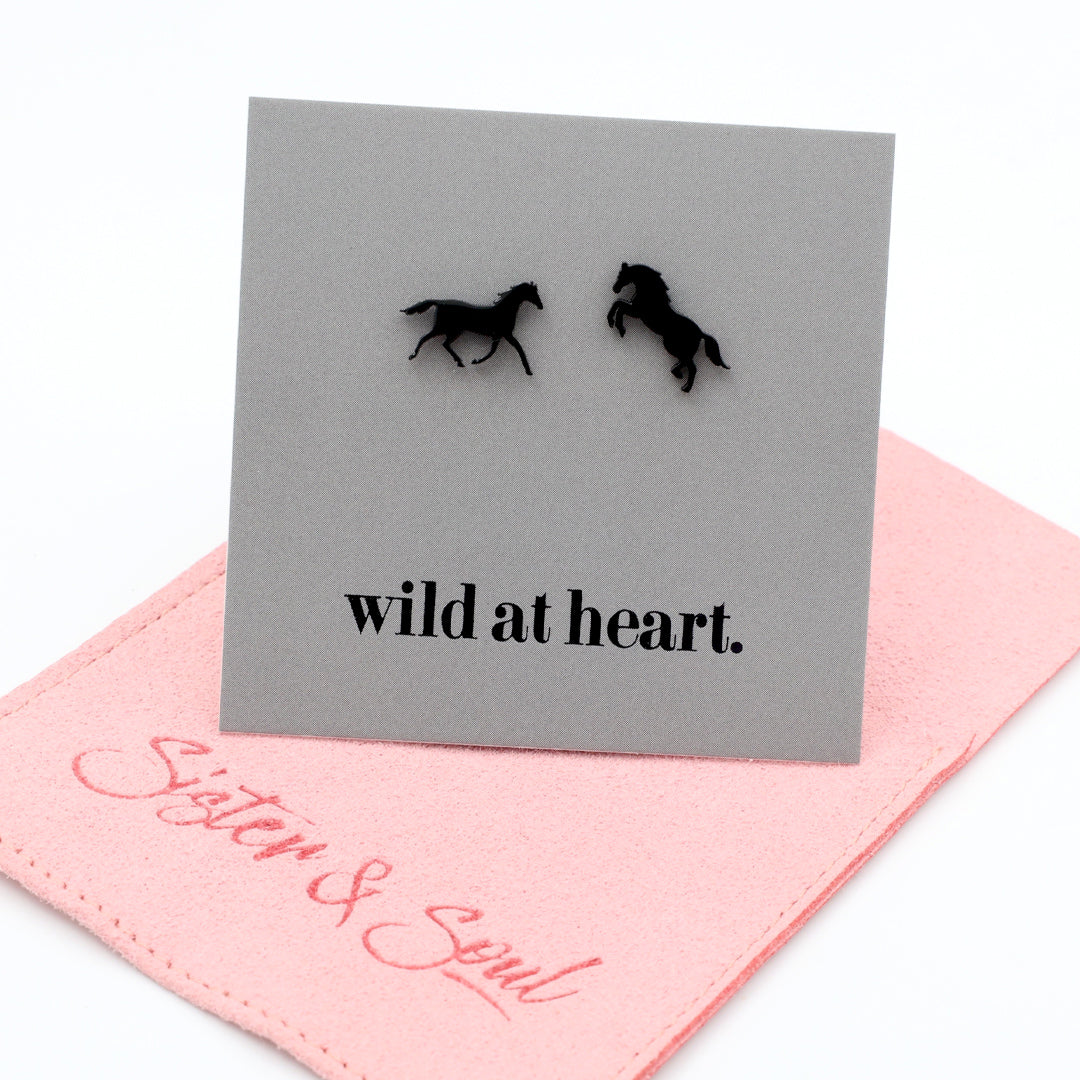Black horse earrings on a black card with 'wild at heart.' text on a pink pouch