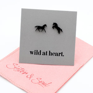 Black horse earrings on a black card with 'wild at heart.' text on a pink pouch