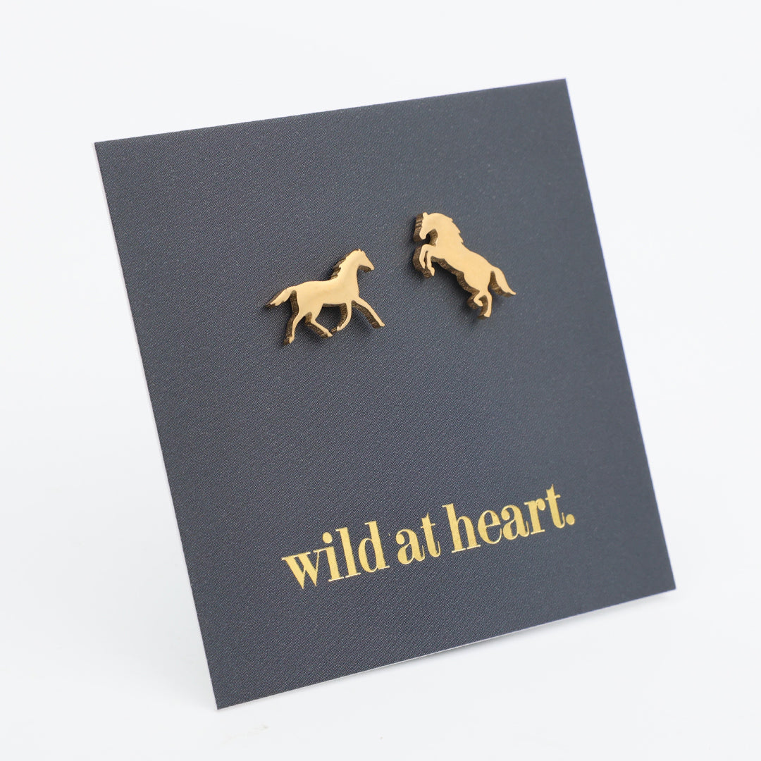 Gold horse earrings on a black card with 'wild at heart.' text 