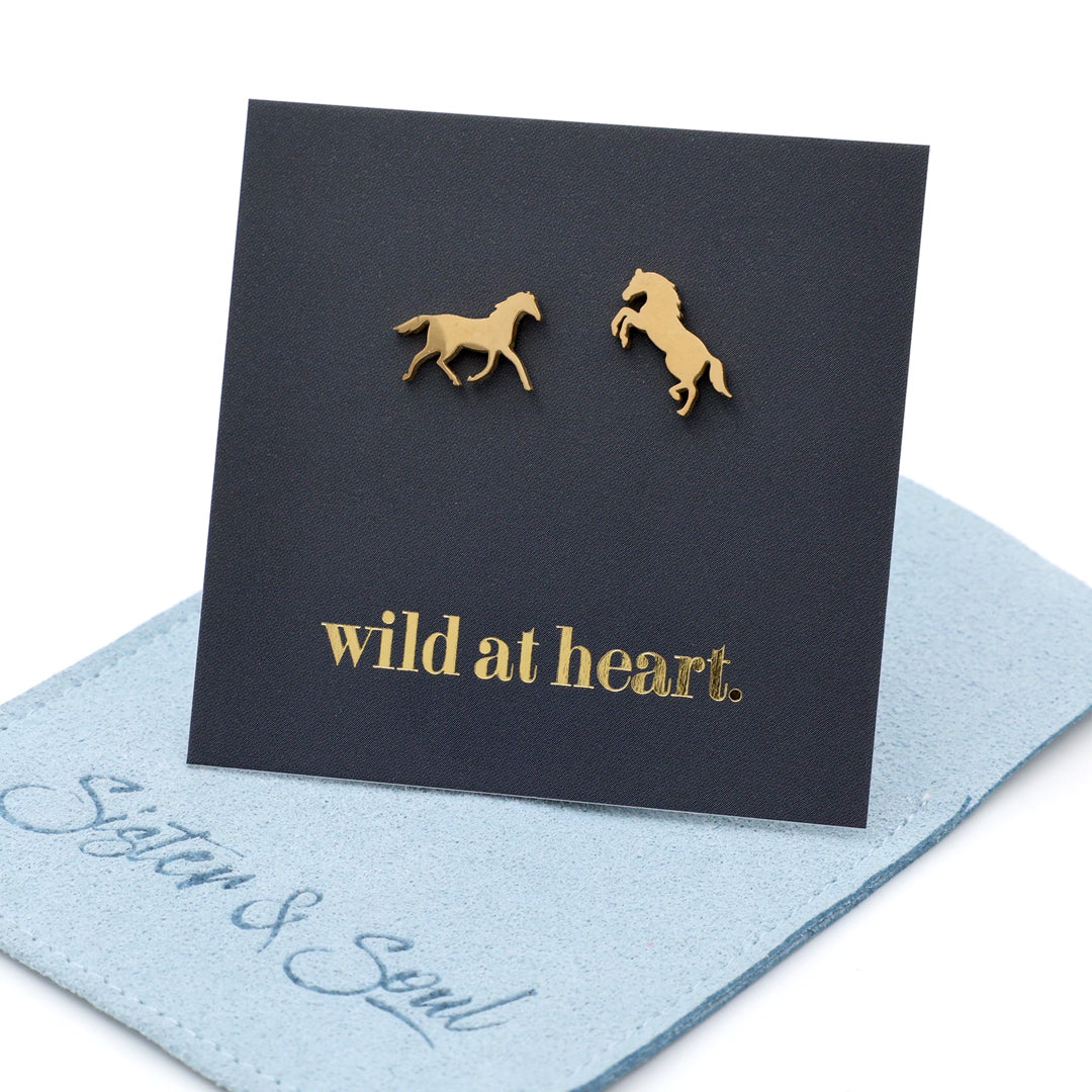 Gold horse earrings on a black card with 'wild at heart.' text on a blue pouch