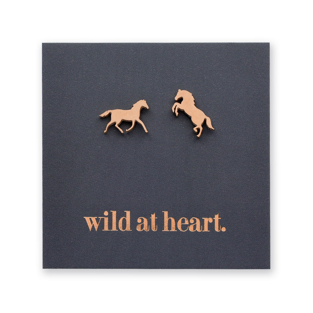 Rose gold horse earrings on a black card with 'wild at heart.' text
