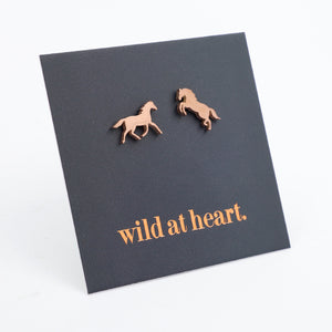 Rose gold horse earrings on a black card with 'wild at heart.' text