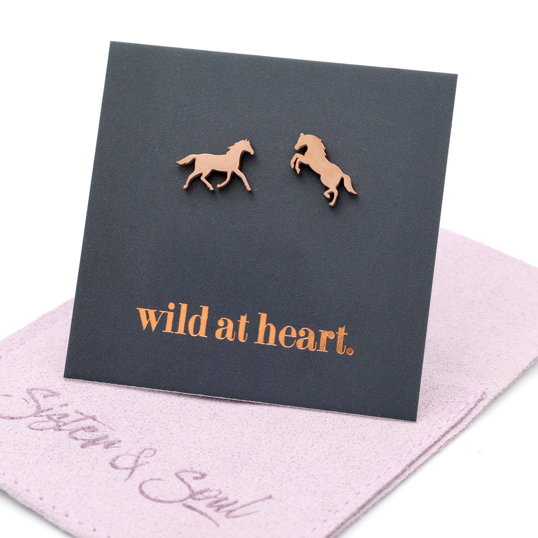 rose gold horse earrings on a black card with 'wild at heart.' text on a mauve pouch