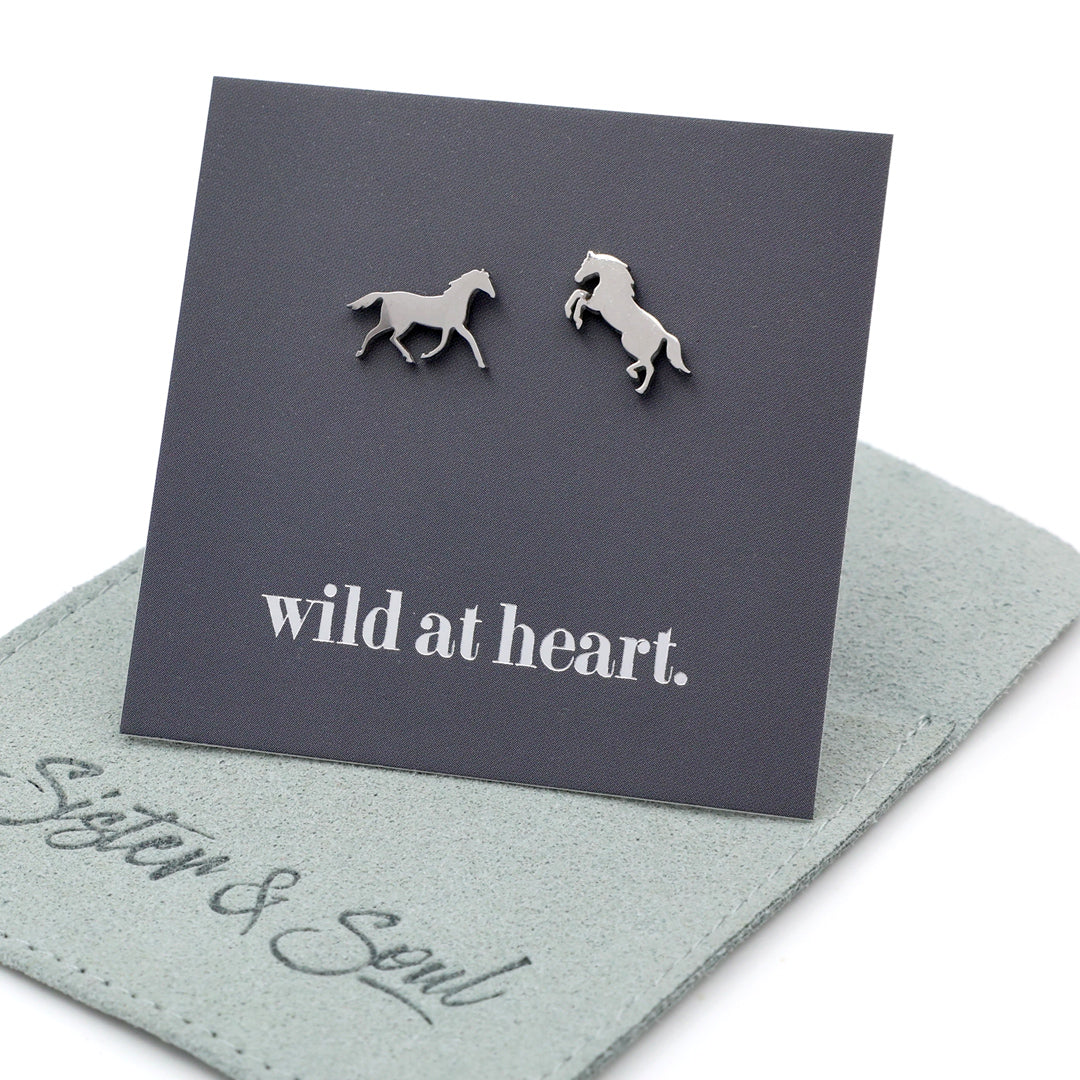 Silver horse earrings on a black card with 'wild at heart.' text on a sage pouch