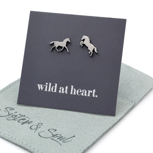Silver horse earrings on a black card with 'wild at heart.' text on a sage pouch