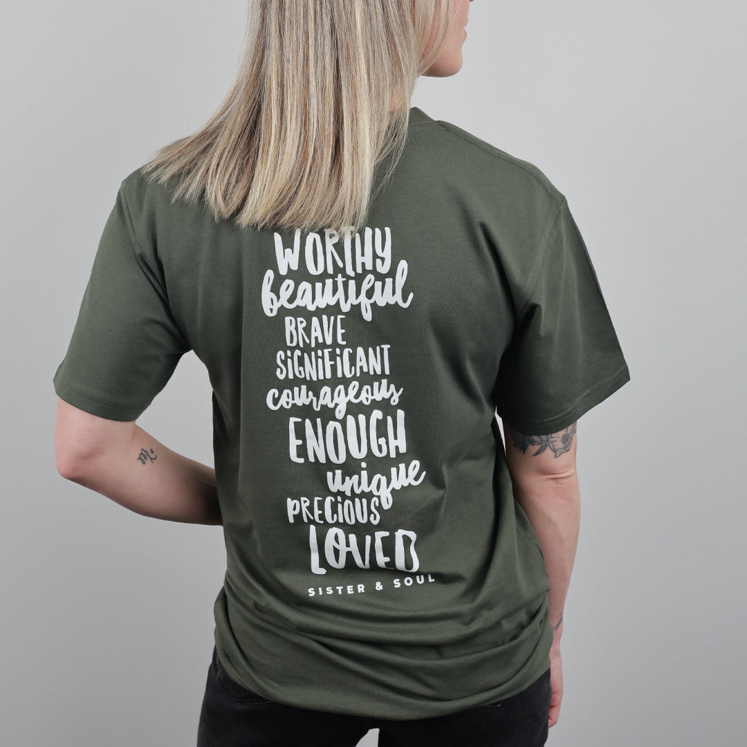 A woman shown from the back wearing an olive green t-shirt with white hand-drawn style text listing positive adjectives and the phrase 'SISTER & SOUL' on the back, against a plain gray background.