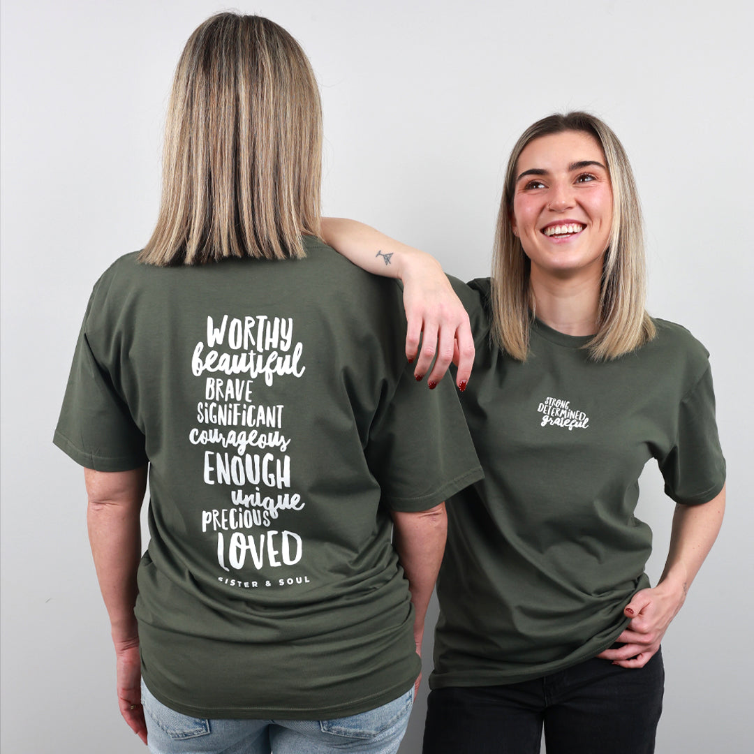 Two women modeling an olive green t-shirt, showing both the front and back views. The back of the shirt features a large white typographic quote, while the front has a smaller matching chest print.