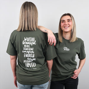 Two women modeling an olive green t-shirt, showing both the front and back views. The back of the shirt features a large white typographic quote, while the front has a smaller matching chest print.