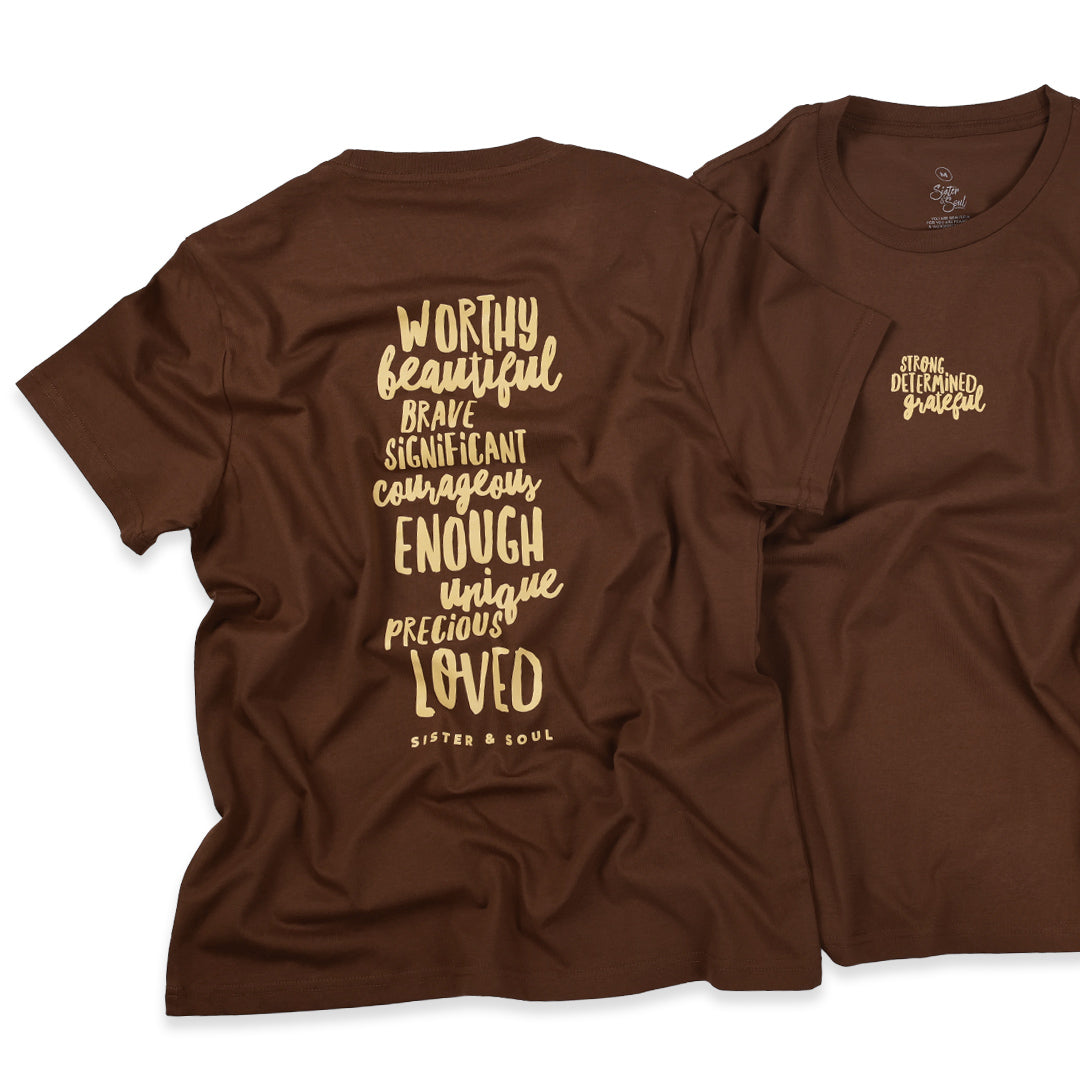 Two brown short-sleeve T-shirts shown on a white background, with the back view on the left and the front view on the right. The back shirt features large gold text listing qualities such as worthy, beautiful, brave, significant, courageous, enough, unique, precious, loved, and 'Sisters & Soul.