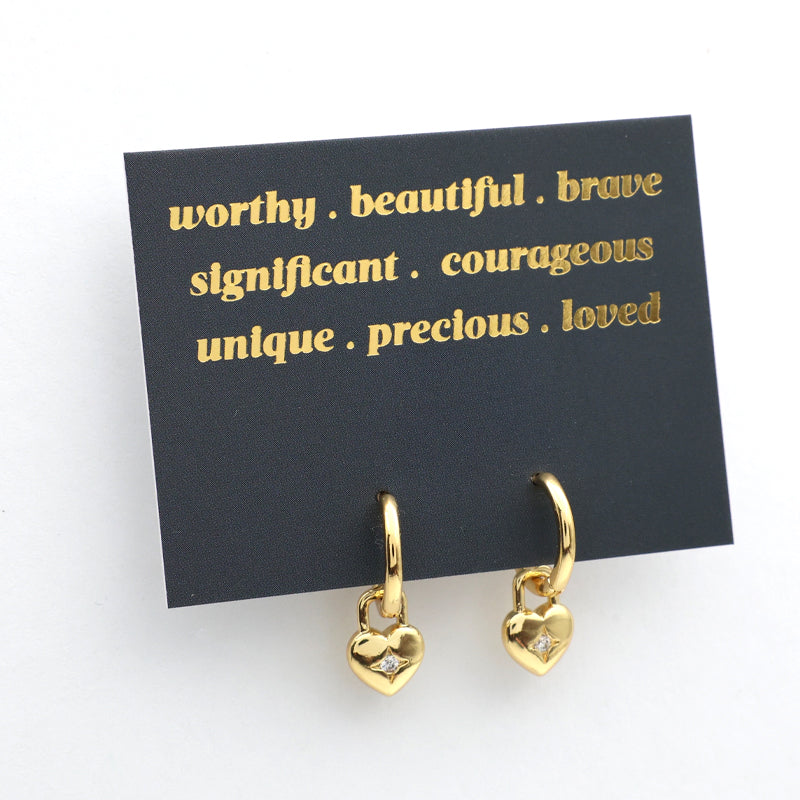 Gold heart-shaped earrings on a black card with gold text